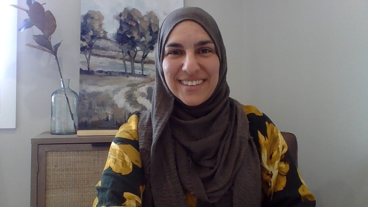 Amany Suleiman smiling, seated in a sunlit room beside a landscape painting and a glass vase